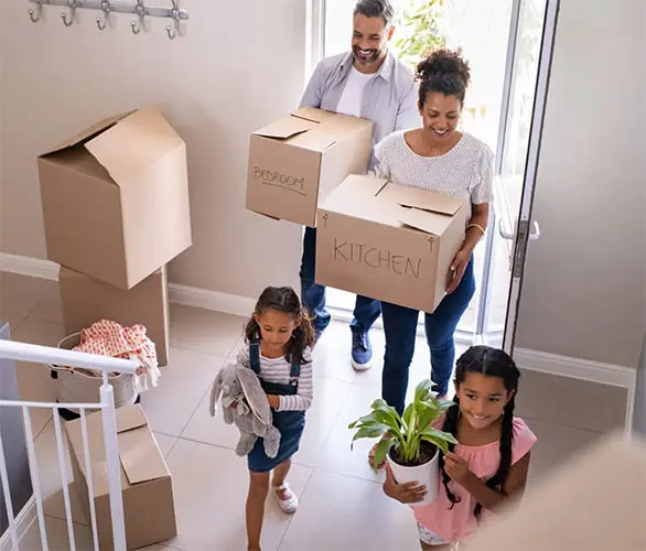 Ethnic family with two children carrying boxes and plant in new home on moving day. High angle view of happy smiling daughters helping mother and father with cardboard boxes in new house. Top view of excited kids having fun walking up stairs running to their rooms while parents holding boxes.