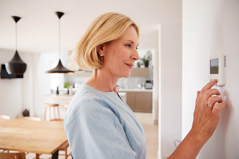 woman adjusting her thermostat thanks to HVAC Direct Mail Marketing
