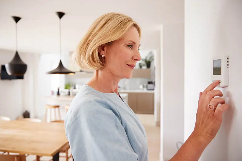 woman adjusting her thermostat thanks to HVAC Direct Mail Marketing