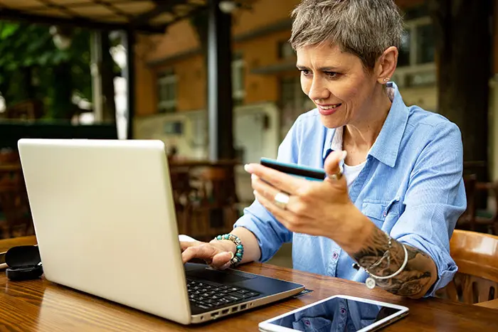 Woman with blue shirt and short hair is sitting at coffee shop and purchasing online