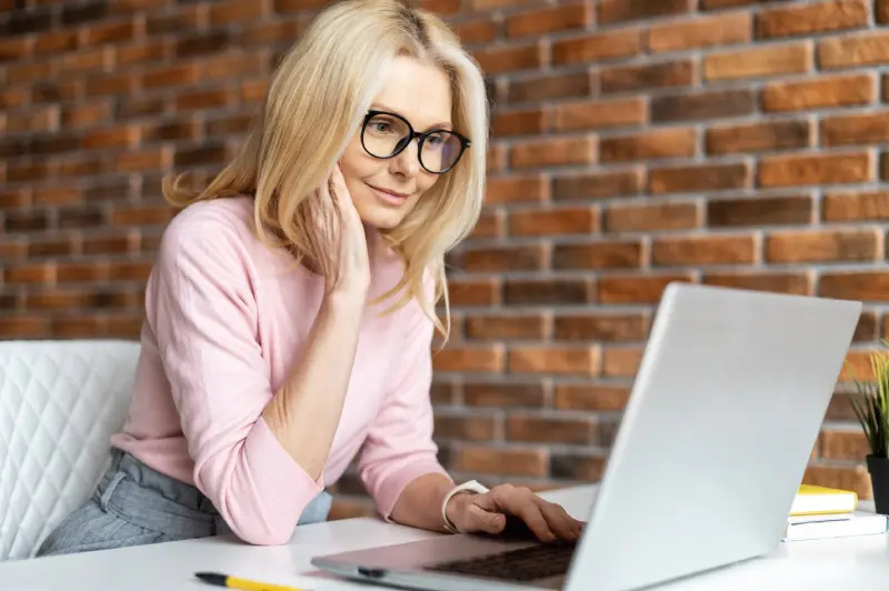 A blonde woman with a brick background on a computer