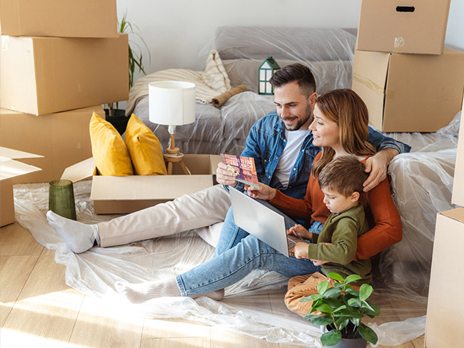 A family sitting down in their new house with boxes on the floor, looking at a Church mailer