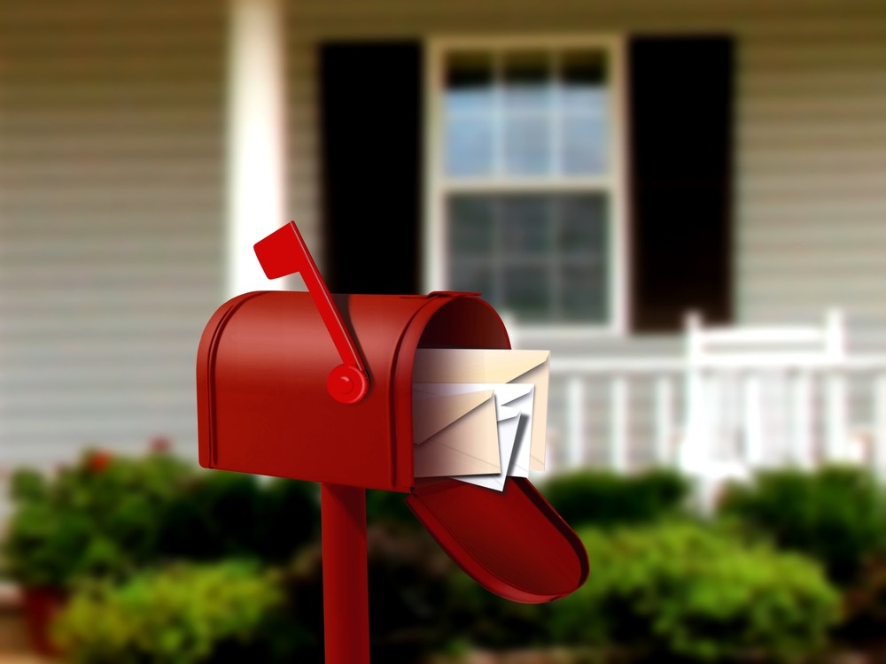 A mailbox in front of a house with letters and postcards.