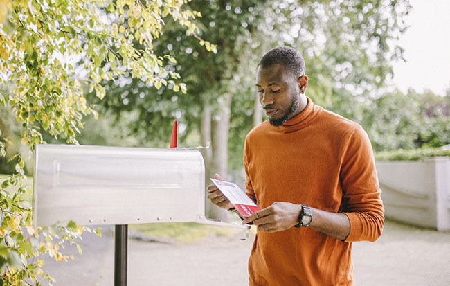 a man in an orange shirt reading mail at the mailbox